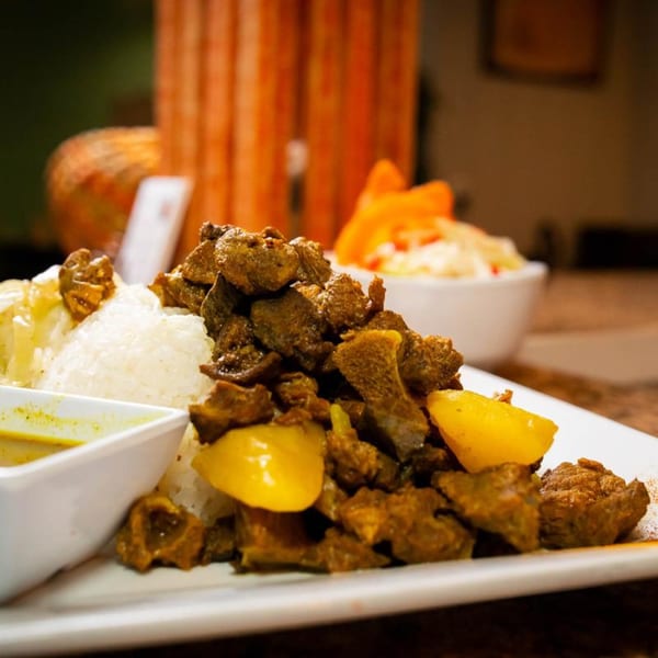 Close-up of Jamaican curry goat with white rice, yellow peppers, and a side of sauce.