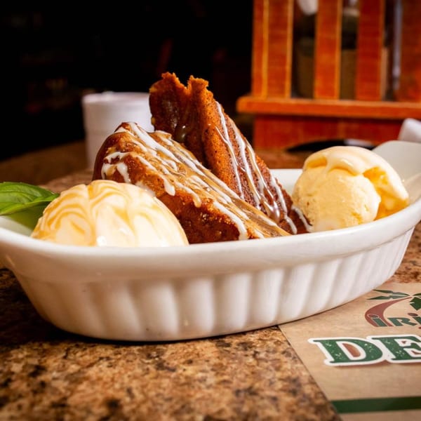 Two slices of Jamaican rum cake with white icing and two scoops of vanilla ice cream.