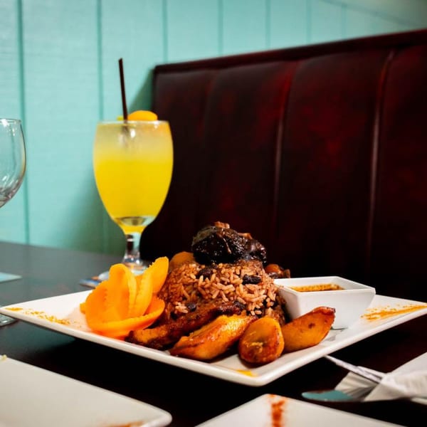A Jamaican meal with rice, plantains, and meat, served with a yellow drink.