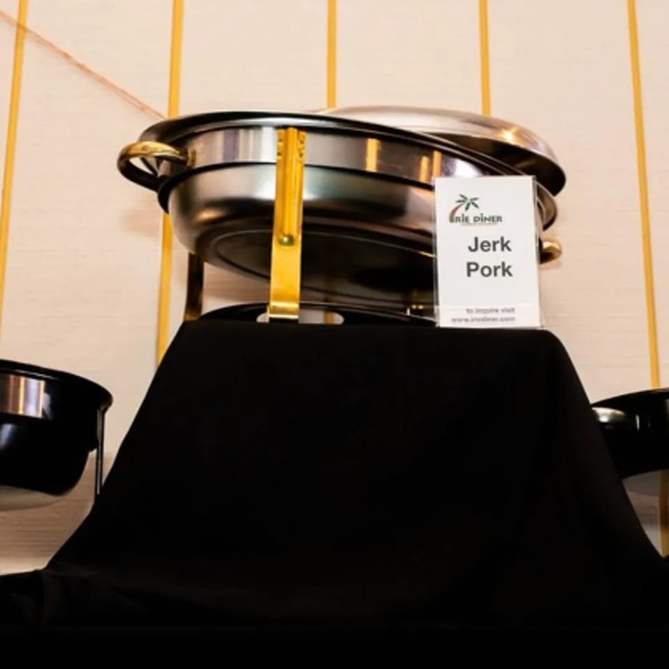 A chafing dish with "Jerk Pork" label from Irie Diner Caribbean Restaurant on a black tablecloth.