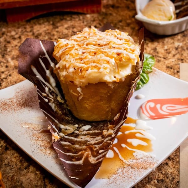 A Jamaican dessert, a fried dumpling topped with coconut flakes and caramel, on a white plate.