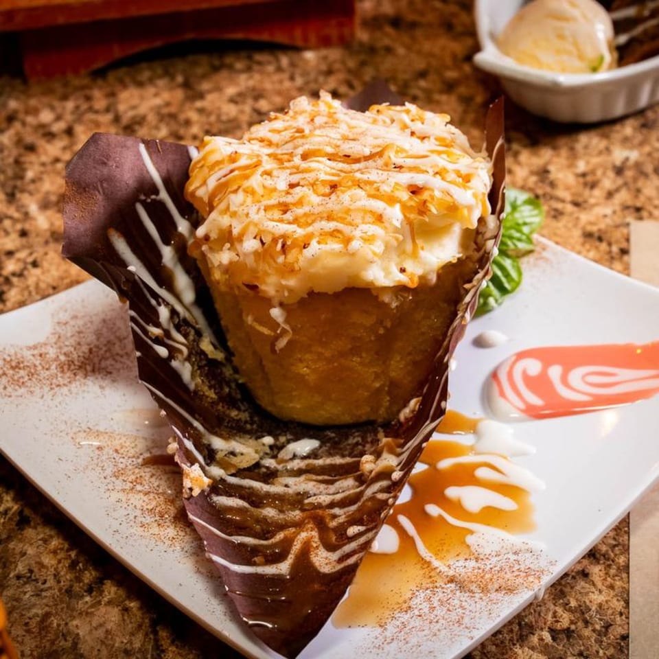 A Jamaican dessert, a fried dumpling topped with coconut flakes and caramel, on a white plate.