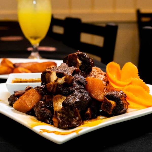 Irie Diner's Jamaican oxtail stew with rice, plantains, and mango slices, alongside a drink.