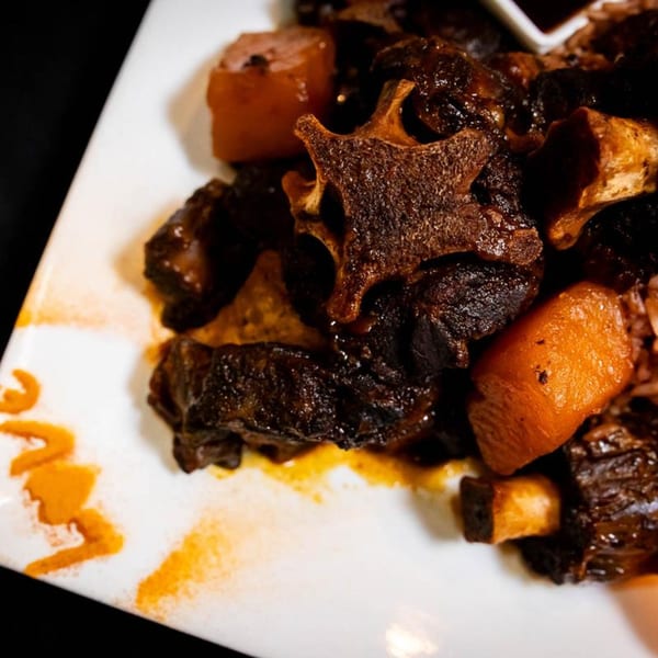 Close-up of Jamaican oxtail stew with carrots on a white plate, with "Love" written in sauce.
