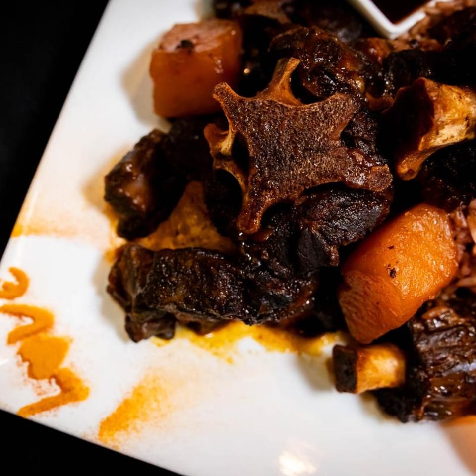 Close-up of Jamaican oxtail stew with carrots on a white plate, with "Love" written in sauce.