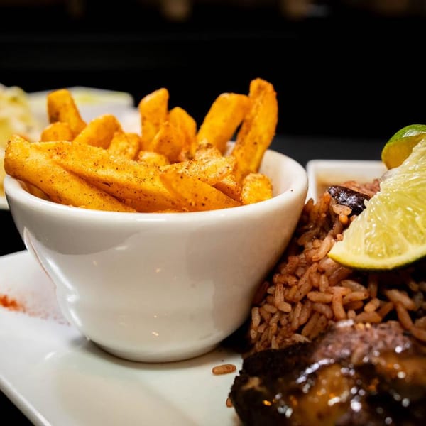 A white bowl of seasoned fries next to Jamaican rice and peas with a lime wedge.
