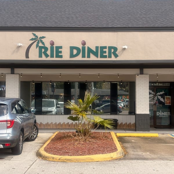 Exterior of Irie Diner Caribbean Restaurant with a palm tree logo, large windows, and a small palm plant.
