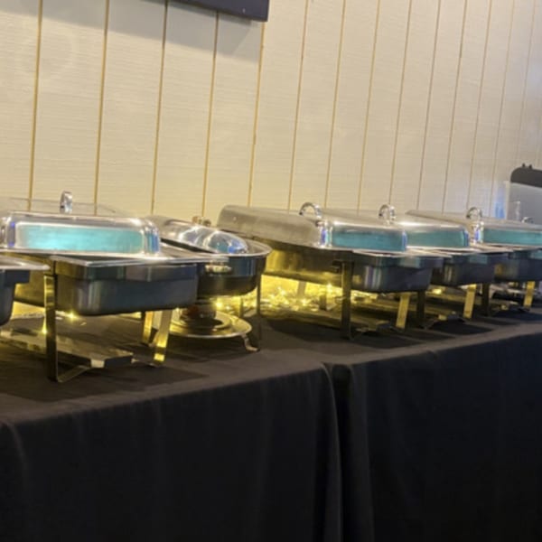 A row of chafing dishes on a black tablecloth, ready for a Jamaican buffet.