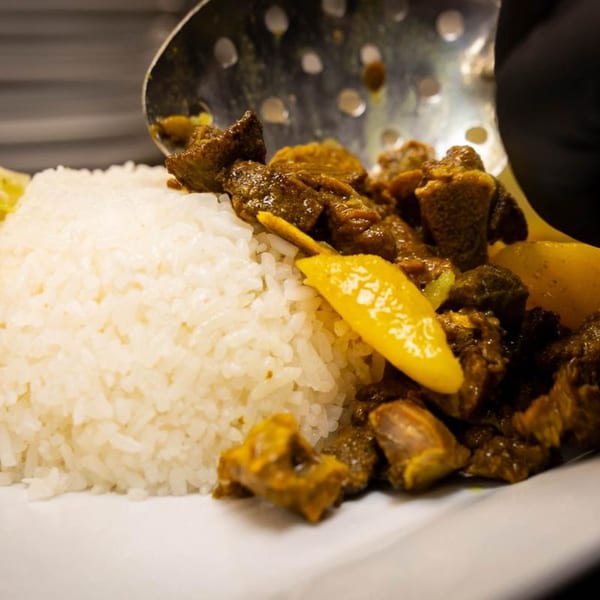 A serving of Jamaican curry goat with white rice and yellow peppers on a white plate.
